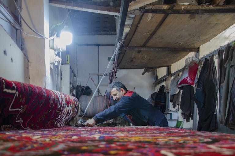 A craftsman weaving a vibrant Persian rug in a traditional workshop in Tabriz, Iran.