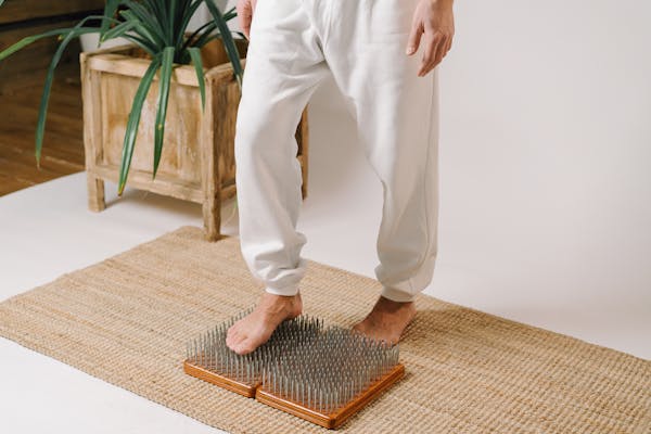 A person in white pants standing on a nail board for meditation and therapy indoors.