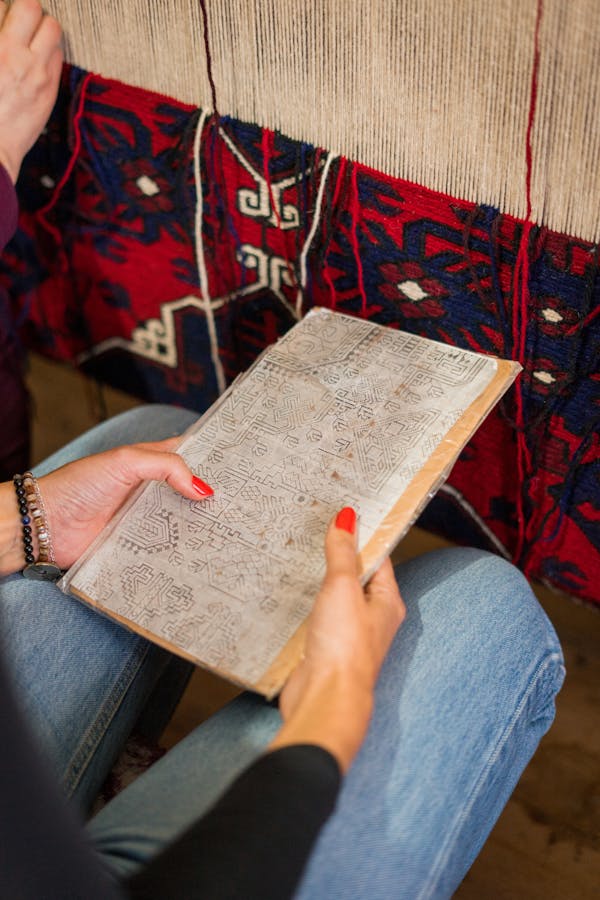 A woman holding a weaving pattern book, showcasing handmade rug creation.